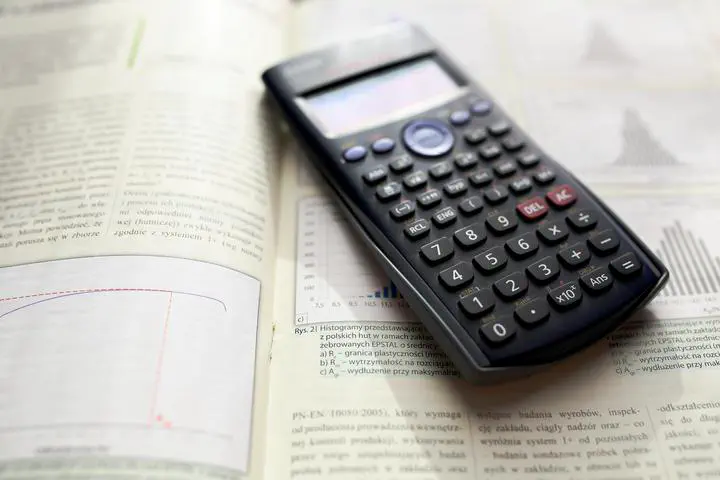 A photograph of a scientific calculator laying on top of a math textbook